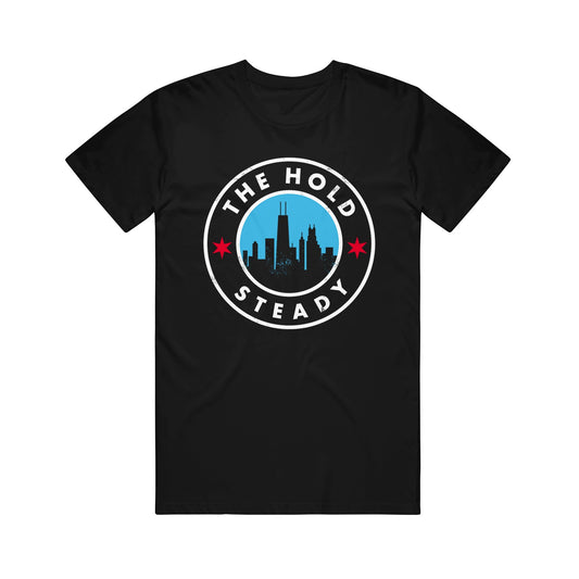 Black Comfort Colors shirt with a circular logo showing a city skyline, two red stars, and "The Hold Steady" in white lettering around the circle.